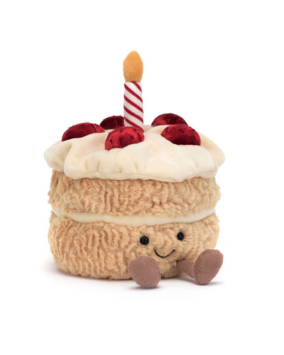 The Jellycat Amuseables Birthday Cake is a plush toy with a smiling face, red cherries on top, white icing, and a red-and-white striped candle with a yellow flame, all perched on small brown legs.