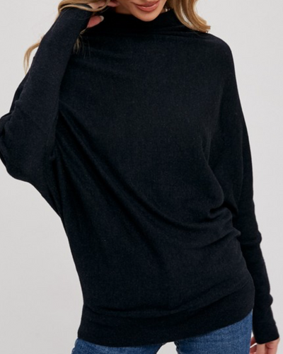 A person in an Ellen Slouch Neck Pullover - Black and blue jeans poses with their hand touching their hair against a plain background.