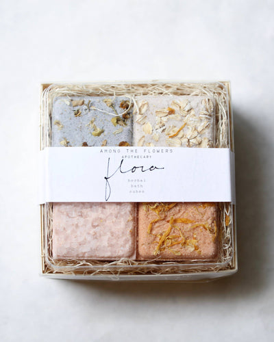 The "Flora Bath Cubes" set from Among the Flowers Apothecary includes four natural fizzers in purple, white, pink, and orange with dried flowers. They are packed in straw-like material and enriched with essential oils for a soothing experience.
