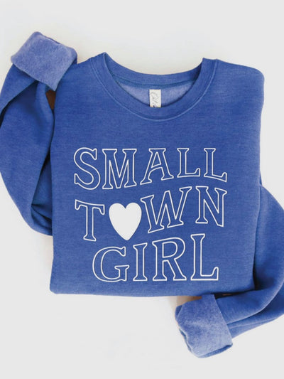 The Small Town Girl Crewneck in Heather Royal features a "SMALL TOWN GIRL" design with a heart replacing the "O" in "TOWN." Cozy and stylish, its sleeves are rolled up, embodying small town love effortlessly on a flat surface.