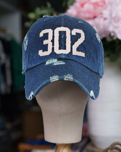 A distressed vintage-inspired baseball hat in Denim Blue with the number '302' embroidered in tan on the front, displayed on a mannequin head.
