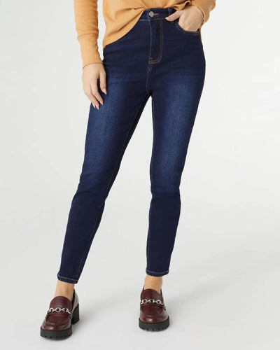 Model wearing dark Everstretch High Rise Skinny Ankle Jeans with a fitted waist, paired with a light tan top. The jeans feature a clean, streamlined silhouette with front pockets and button closure.