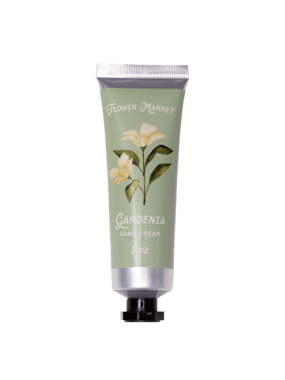 A product image of the Flower Market Gardenia Hand Cream in a 1 oz tube. The packaging features a soft green background with delicate gardenia flower illustrations and text reading "Gardenia Hand Cream." The tube has a silver cap and an elegant, floral-inspired design, perfect for gifting or personal use.