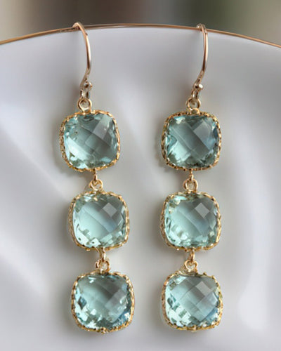 A pair of elegant drop earrings featuring three 9mm prasiolite glass square blocks set in gold-plated bezels with 14k gold-filled earwires. Displayed on a white ceramic dish, these earrings exude timeless sophistication.