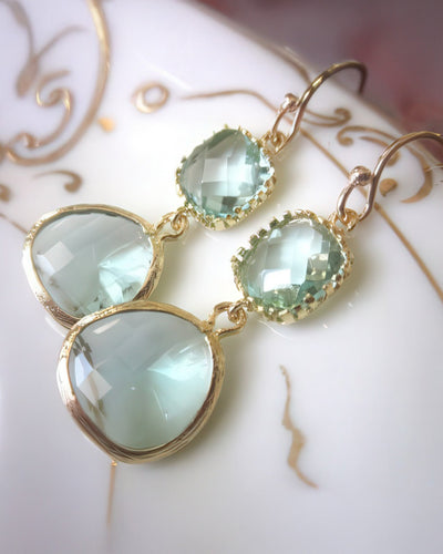 A pair of stunning drop earrings featuring 13mm faceted prasiolite teardrop gems and 9mm square blocks, set in gold-plated bezels with 14k gold-filled earwires. Displayed on a white plate with gold detailing, these earrings radiate elegance and charm.