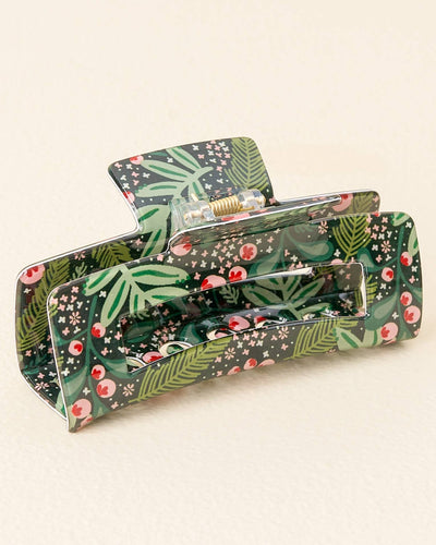 Close-up of a rectangular acrylic hair claw in a dark green, festive holiday pattern featuring foliage and red berries.
