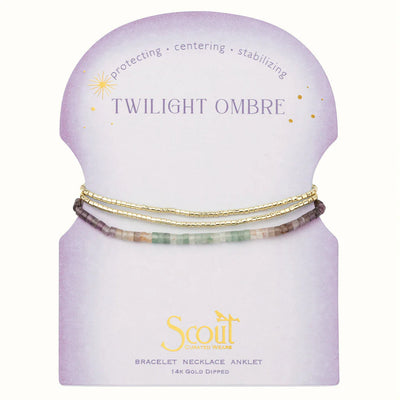 The "Ombre Stone Wrap - Twilight/Gold" set features multicolored bracelets with gold accents on a recycled purple card, labeled "Twilight Ombre." The pastel gradient design includes words like "protecting," "centering," and "stabilizing," with Scout's branding at the bottom.