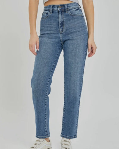 A person showcases the High Rise Mom Jean with Front Pocket Shape in medium denim, standing against a plain background. The focus is on their lower half, displaying the jeans' on-trend and comfortable straight-leg fit paired with white sneakers.