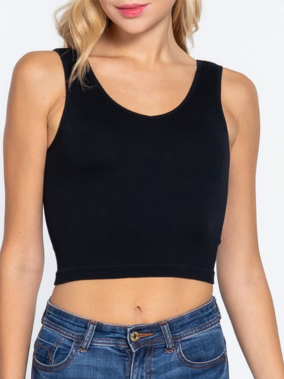 A person is wearing the Amaya Reversible Seamless Crop Tank in black with blue jeans against a white background. The fitted, ribbed fabric provides a casual yet chic look ideal for layering.