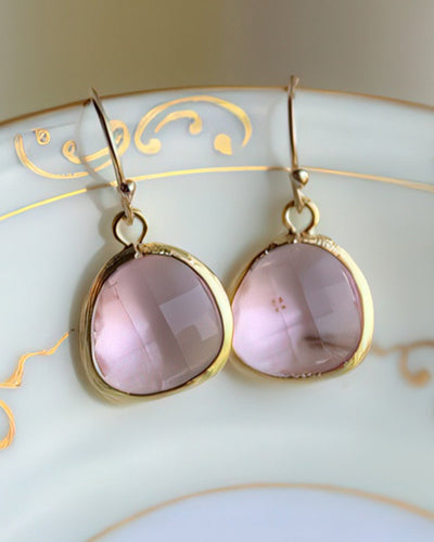 A pair of elegant light pink drop earrings featuring 13mm faceted glass gems set in gold-plated bezels with 14k gold-filled earwires. Displayed on a white ceramic dish with gold detailing, these earrings exude timeless simplicity and grace.