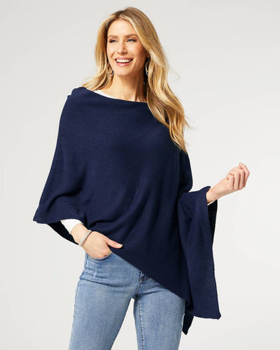 A woman wearing a navy lightweight poncho styled asymmetrically over a white top and blue jeans. The soft, flowing fabric drapes elegantly, showcasing its versatile and relaxed fit. She is smiling confidently, accessorized with silver hoop earrings and a bracelet.