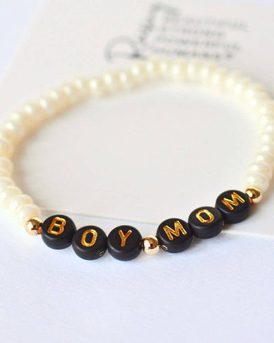 The Boy Mom Beaded Stretch Bracelet – Black and Gold features elegant pearl beads interwoven with black ones, proudly displaying golden letters that spell "BOY MOM" on a pristine white background.