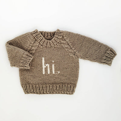 Hand-knit baby and toddler crew neck sweater in pebble-colored yarn with 'hi.' knitted in white on the front, featuring cable trim raglan sleeves and ribbed cuffs.