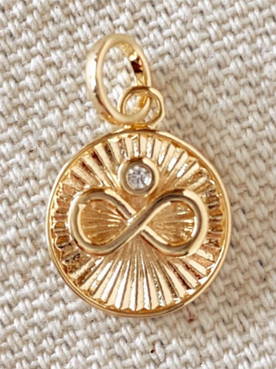 The 18K Gold Filled Infinity Charm Pendant with Solitaire Cubic Zirconia features a raised infinity symbol and a sparkling cubic zirconia on a textured beige backdrop, with radiant lines in its circular design adding elegance to this timeless piece.