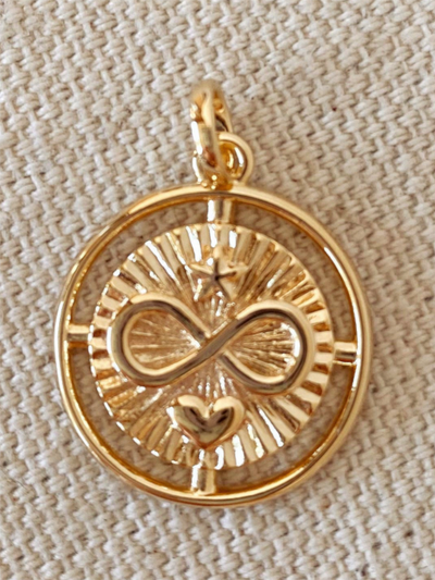 The 18K Gold Filled Heart Star Infinity Love Charm is a circular pendant crafted in gold filled with an elegant infinity symbol at the center, surrounded by a starburst design and a small heart beneath on a textured beige background.