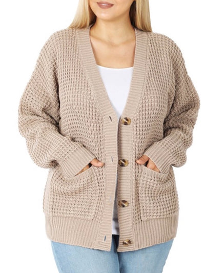 The person is wearing the Avery Button Cardigan in Heather Beige, featuring a textured knit, large buttons, and pockets—perfect for fall and winter layering over a white shirt. The casual ensemble is completed with light blue jeans and long, straight blonde hair.